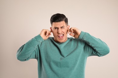 Emotional man covering ears with fingers on beige background