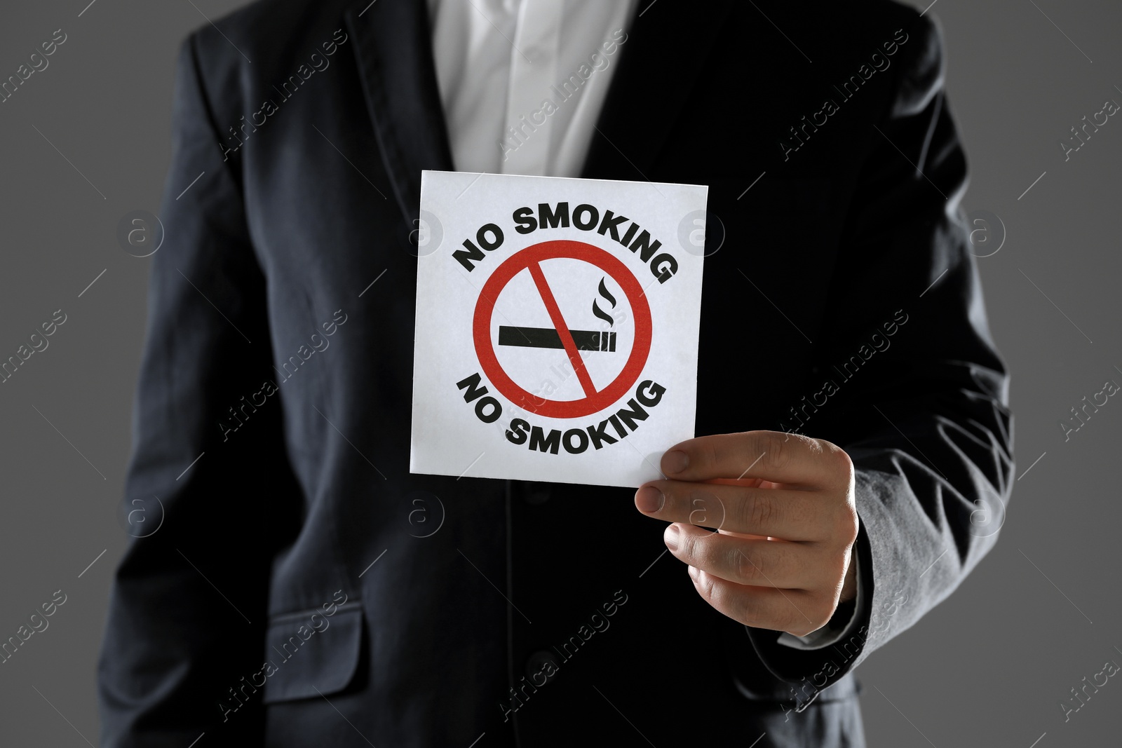 Photo of Man holding card with no smoking sign on gray background, closeup