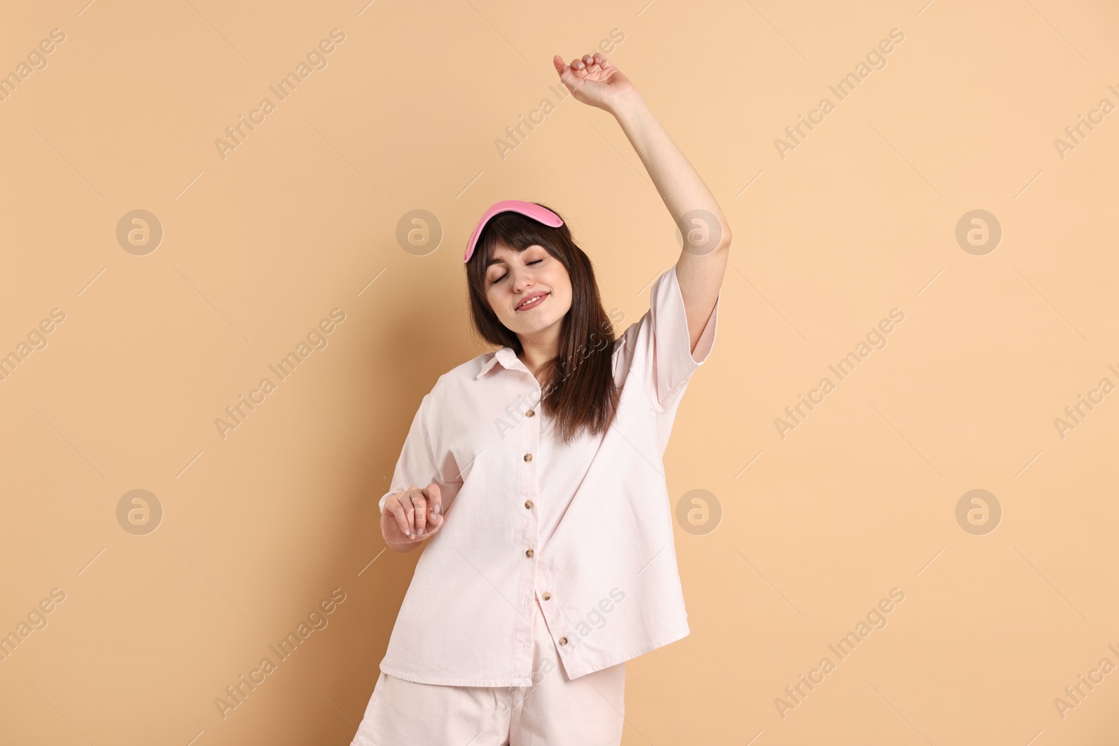 Photo of Woman in pyjama and sleep mask stretching on beige background