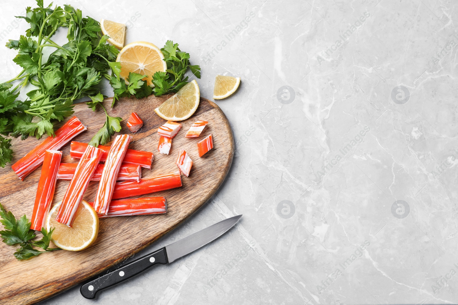 Photo of Delicious crab sticks with parsley and lemon on light grey marble table, flat lay. Space for text