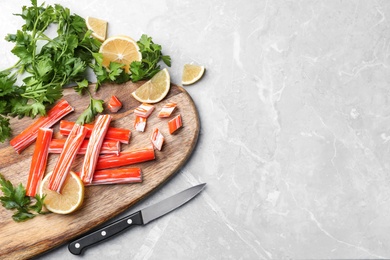 Delicious crab sticks with parsley and lemon on light grey marble table, flat lay. Space for text
