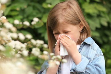 Photo of Little girl suffering from seasonal pollen allergy near blossoming tree on spring day