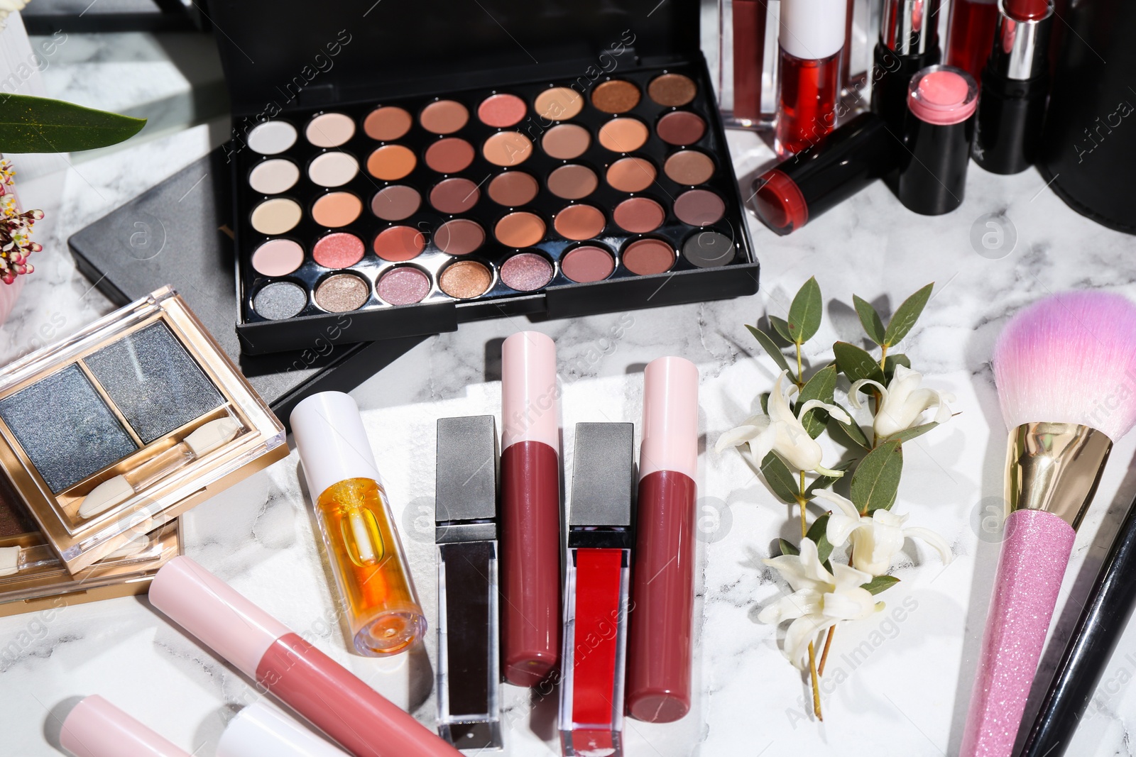 Photo of Bright lip glosses among different cosmetic products on white dressing table