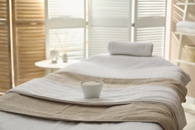 Photo of Massage table with soft towels and sea salt in spa salon