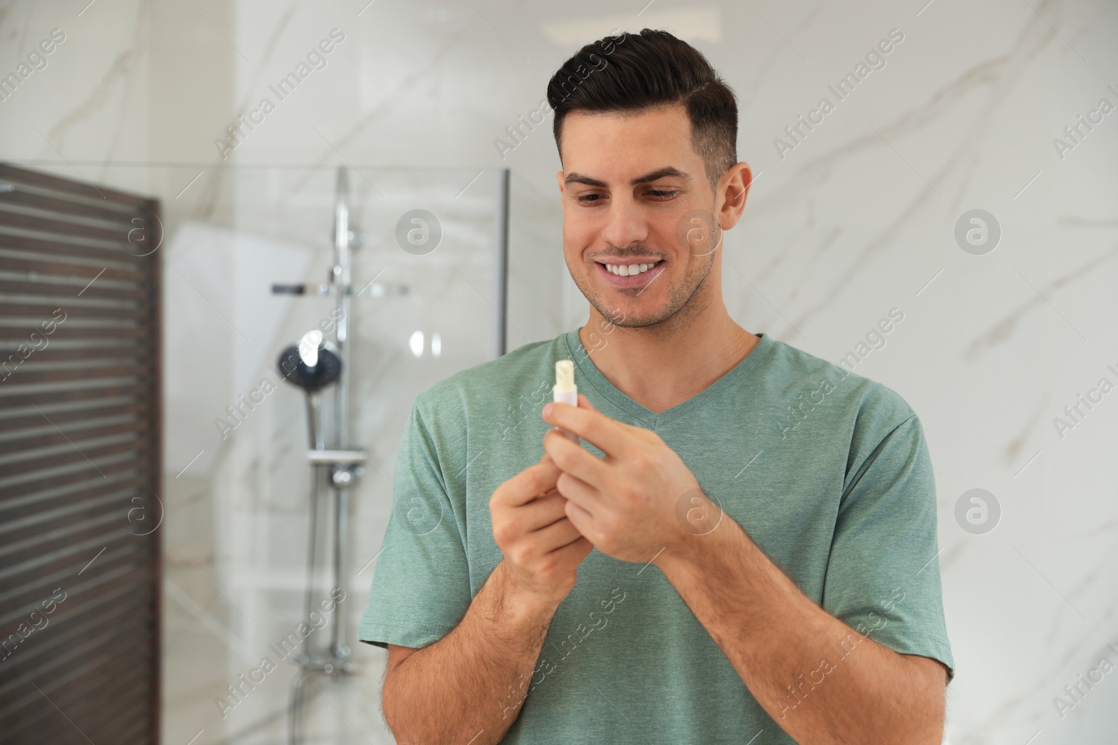 Photo of Man applying hygienic lip balm in bathroom