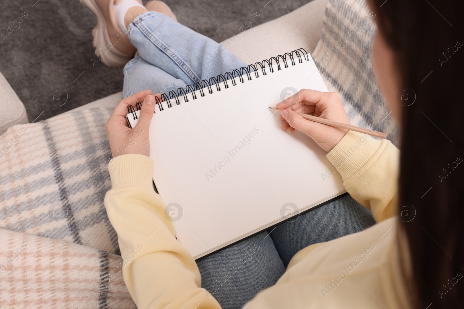 Photo of Young woman drawing in sketchbook on sofa, above view