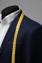 Photo of Semi-ready jacket with tailor's measuring tape on mannequin, closeup