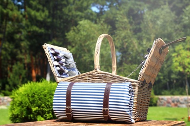 Picnic basket with blanket on wooden table in garden