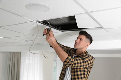 Photo of Man with pliers repairing ceiling wiring indoors