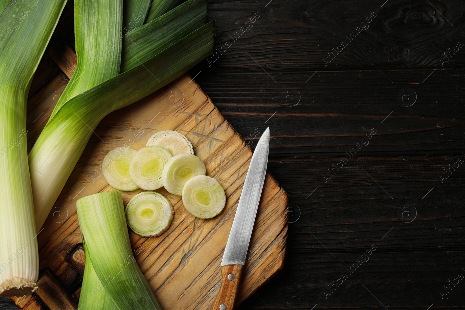 Photo of Fresh raw leeks on black wooden table, flat lay. Ripe onion