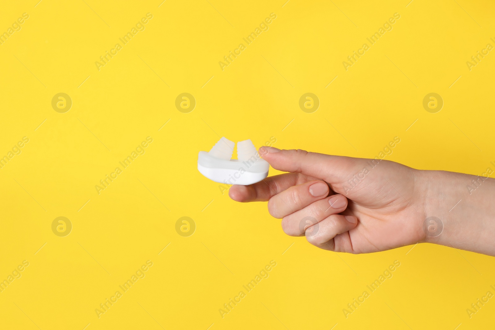 Photo of Woman holding anti-snoring device on yellow background, closeup. Space for text