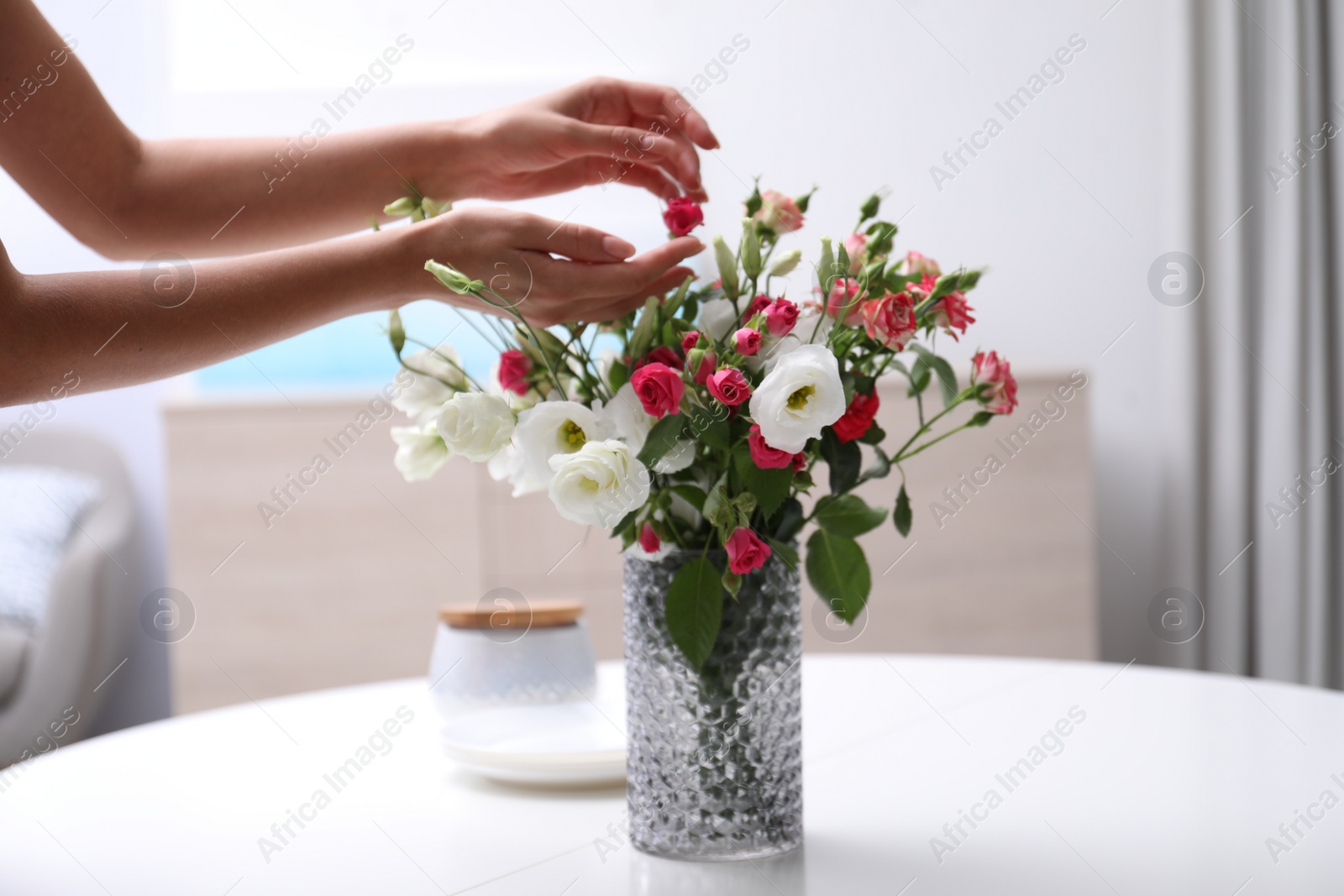 Photo of Woman and vase with beautiful flowers on white table in room, closeup