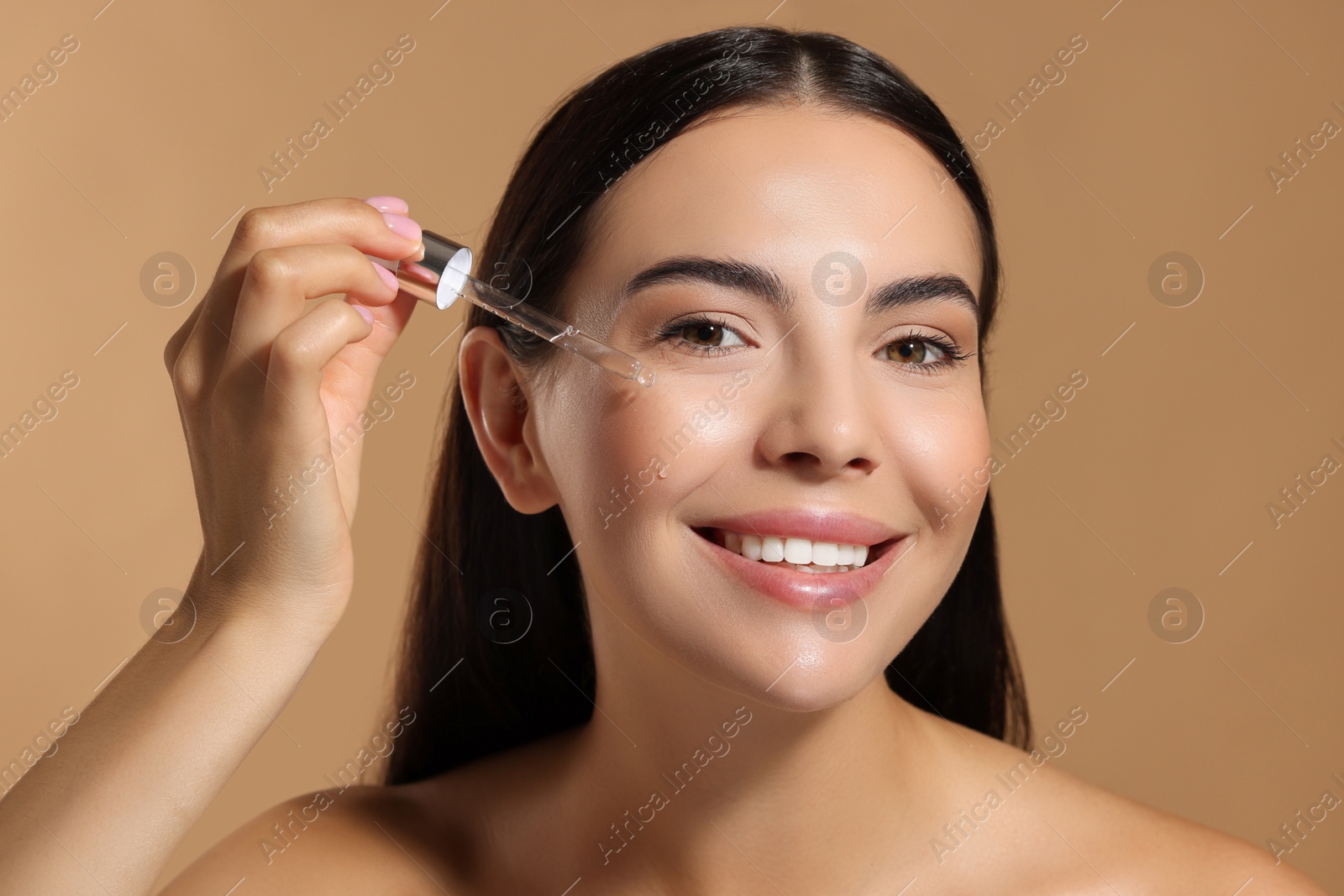 Photo of Beautiful young woman applying serum onto her face on beige background