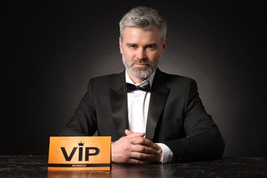 Photo of Handsome man sitting at table with VIP sign on black background