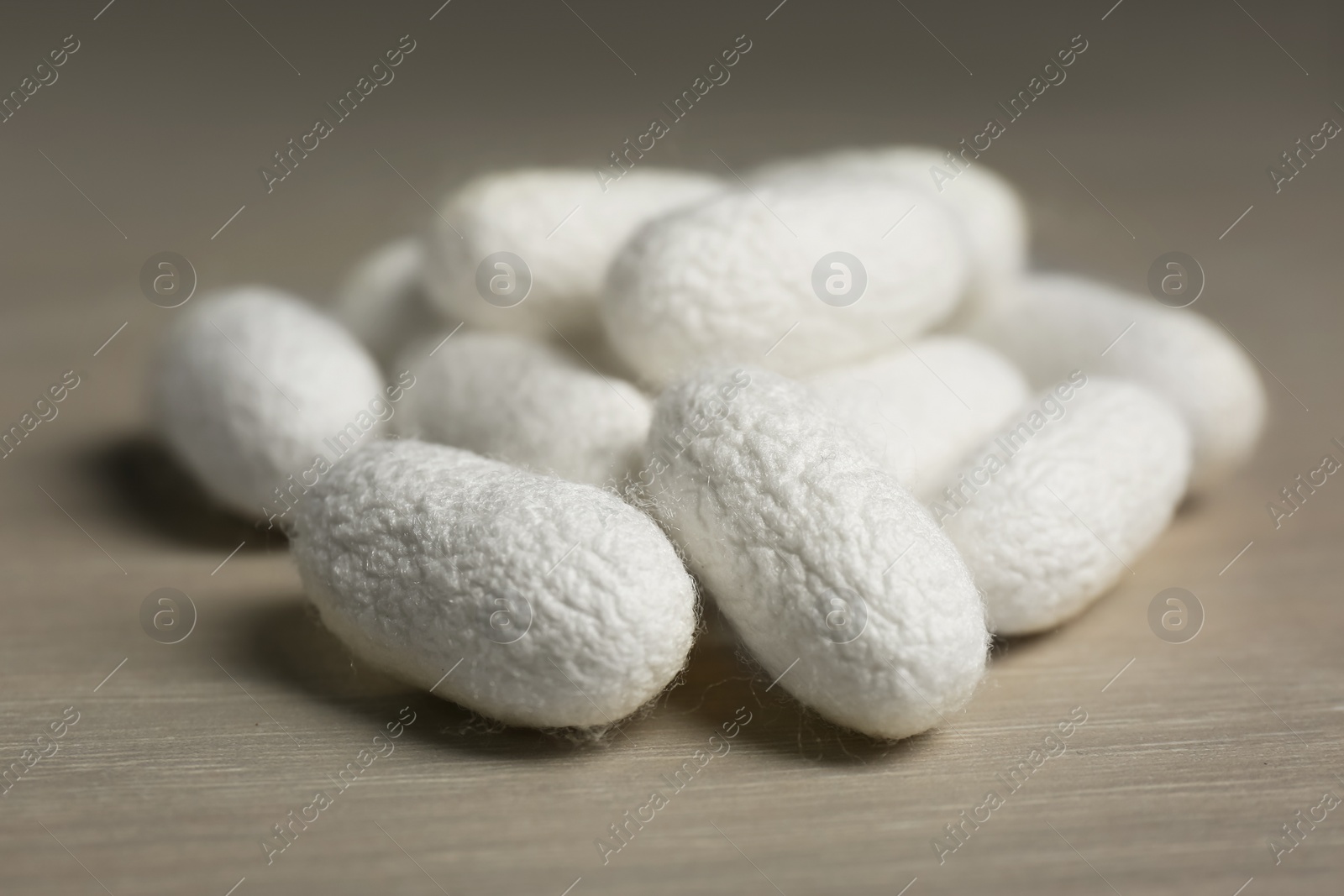 Photo of Heap of white silk cocoons on wooden table, closeup