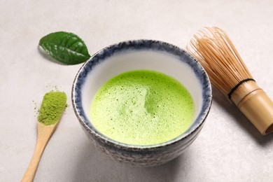 Photo of Cup of matcha tea, bamboo tools and green powder on light gray table, closeup