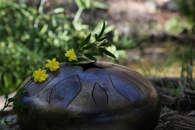 Photo of Steel tongue drum and yellow flowers outdoors. Percussion musical instrument