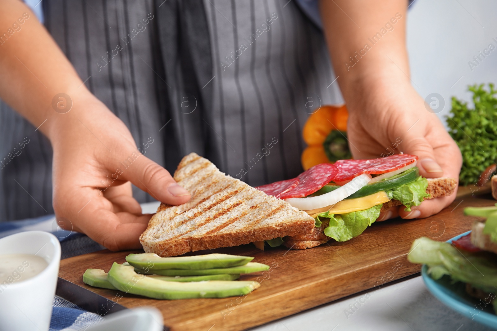 Photo of Woman making tasty sandwich with sausage at  white table, closeup