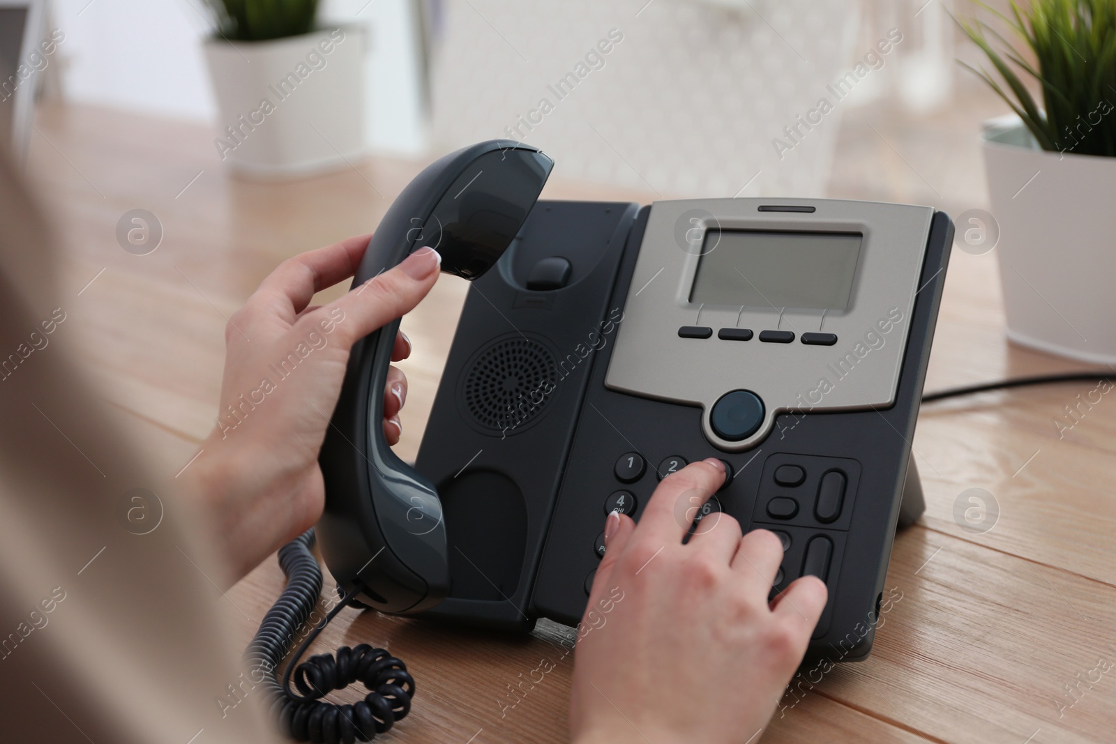 Photo of Woman using desktop telephone at wooden table in office, closeup. Hotline service