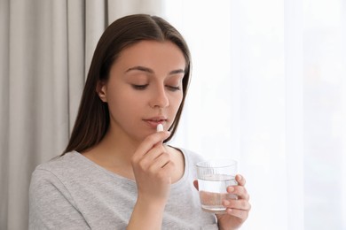 Photo of Young woman with glass of water taking pill at home