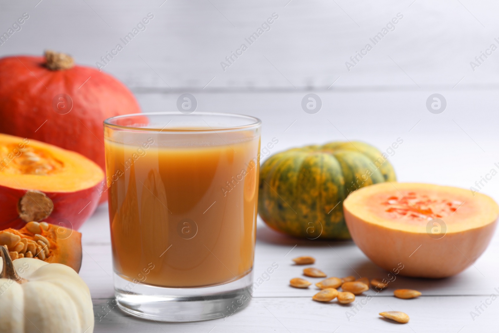 Photo of Tasty pumpkin juice in glass and different pumpkins on white wooden table