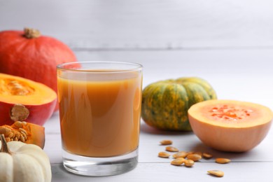 Photo of Tasty pumpkin juice in glass and different pumpkins on white wooden table