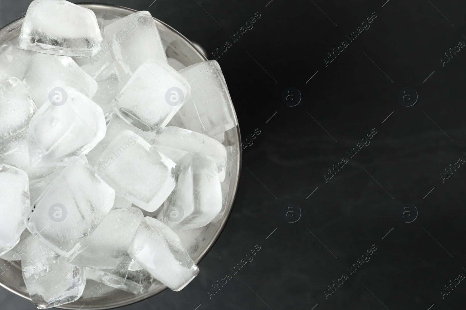 Photo of Metal bucket with ice cubes on black background, top view. Space for text