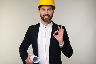 Photo of Architect in hard hat with draft showing OK gesture on gray background