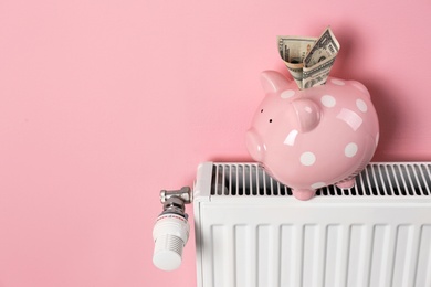 Photo of Heating radiator and piggy bank with money on color background. Space for text