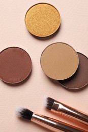 Photo of Different beautiful eye shadows and makeup brushes on beige background, flat lay