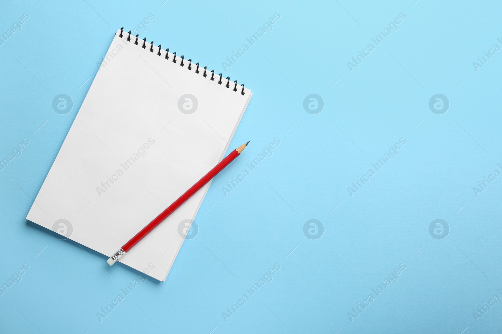 Photo of Notebook and pencil on light blue background, top view. Space for text