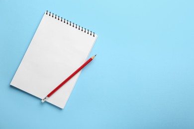 Photo of Notebook and pencil on light blue background, top view. Space for text