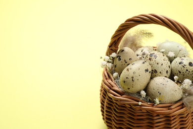 Photo of Quail eggs and flowers in wicker basket on light background, space for text. Easter celebration