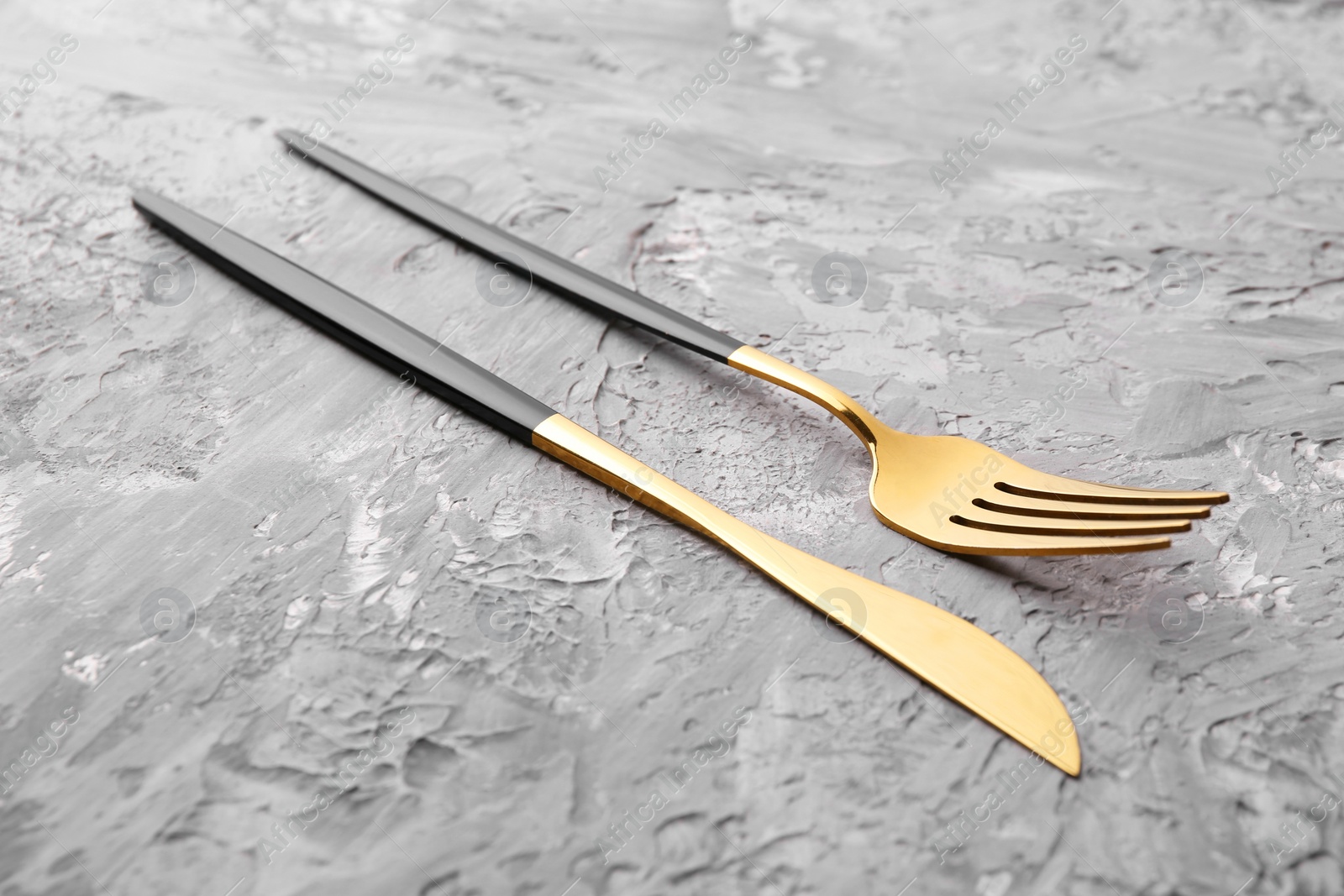 Photo of Elegant cutlery. Stylish knife and fork on grey textured table, closeup
