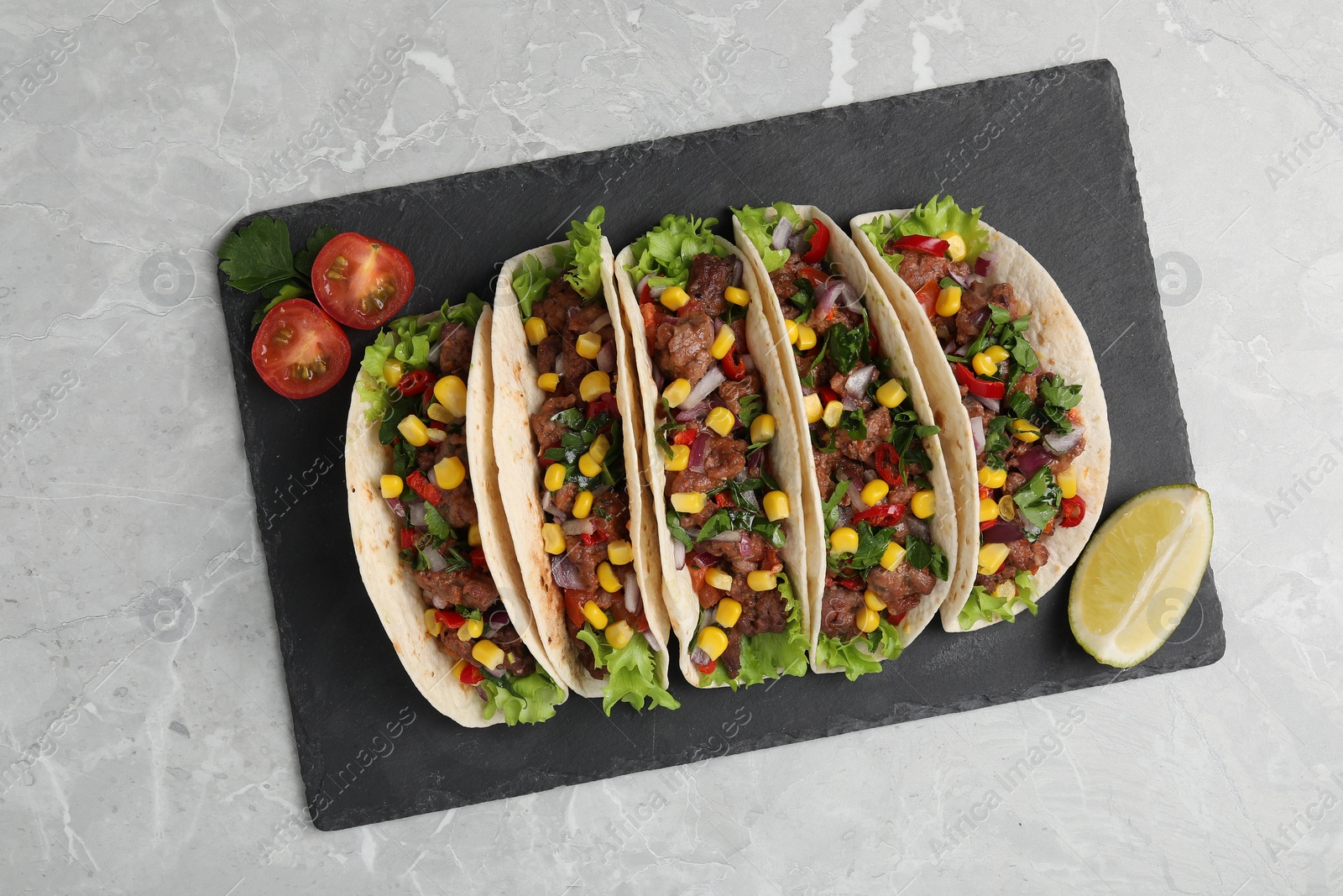 Photo of Delicious tacos with meat, vegetables and lime on light gray marble table, top view