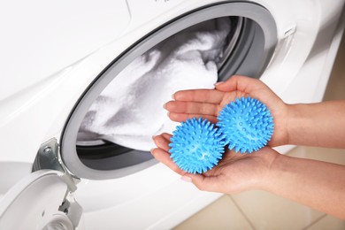 Photo of Woman putting blue dryer balls into washing machine, above view