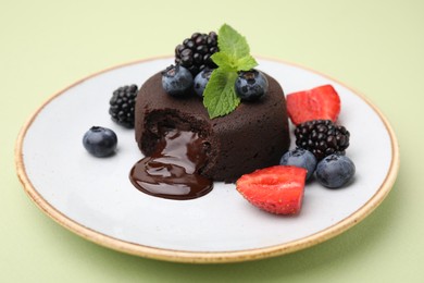Photo of Plate with delicious chocolate fondant, berries and mint on light green table, closeup