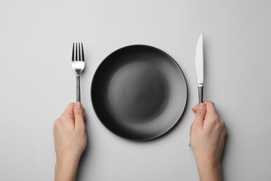 Photo of Woman with fork, knife and empty plate on grey background, top view