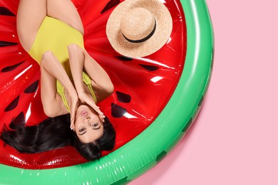 Photo of Young woman wearing stylish swimsuit on inflatable mattress against pink background, above view