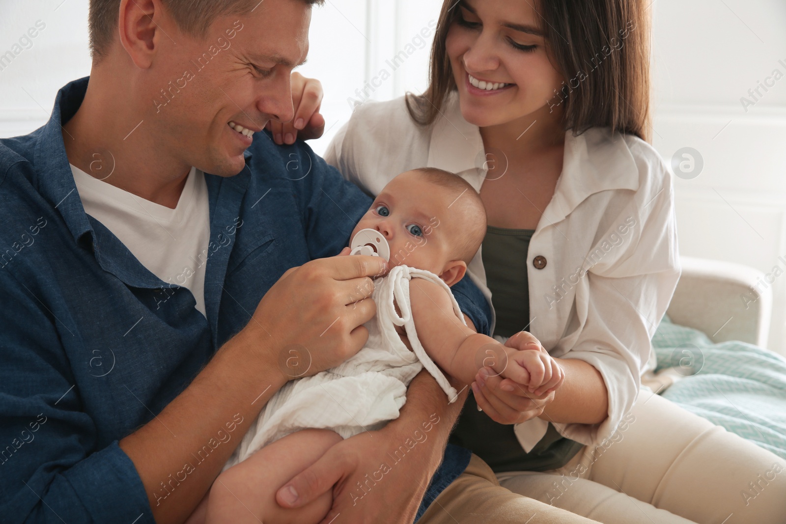 Photo of Happy couple holding their cute little baby with pacifier at home