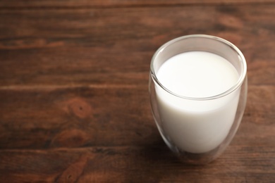 Photo of Glass of fresh milk on wooden table. Space for text