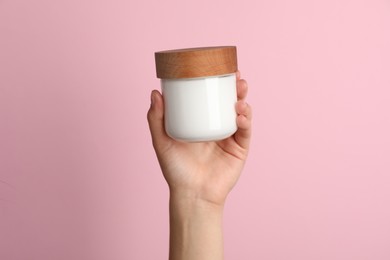 Photo of Woman holding jar of face cream on pink background, closeup