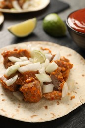 Photo of Delicious taco with vegetables, meat and lime on dark table, closeup