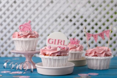 Delicious cupcakes with pink cream and toppers for baby shower on light blue wooden table