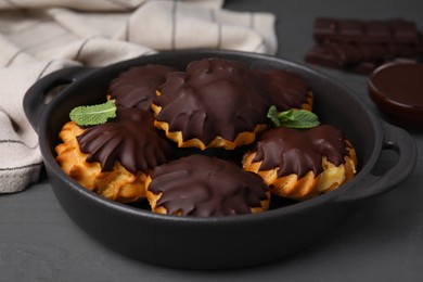 Photo of Delicious profiteroles with chocolate spread and mint in frying pan on grey table, closeup