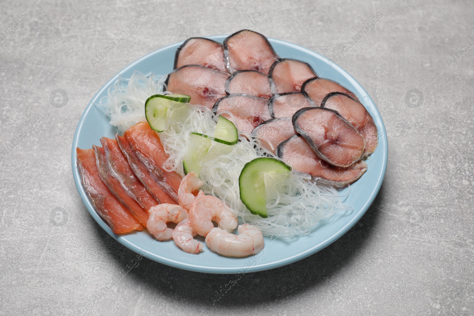 Photo of Set with raw salmon, mackerel slices, shrimps served with cucumber and funchosa on light grey table