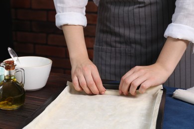 Photo of Woman making delicious baklava at wooden table, closeup