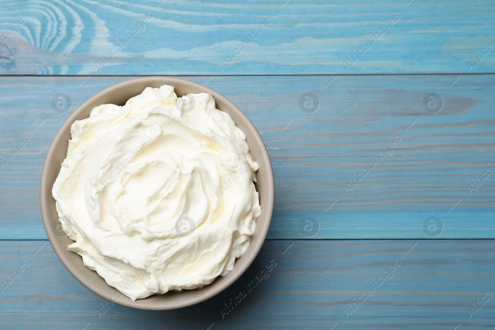 Photo of Bowl of tasty cream cheese on light blue wooden table, top view. Space for text