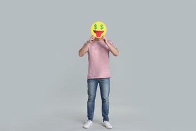 Photo of Man holding emoticon with dollar signs instead of eyes on grey background