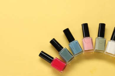 Colorful nail polishes in bottles on yellow background, flat lay. Space for text